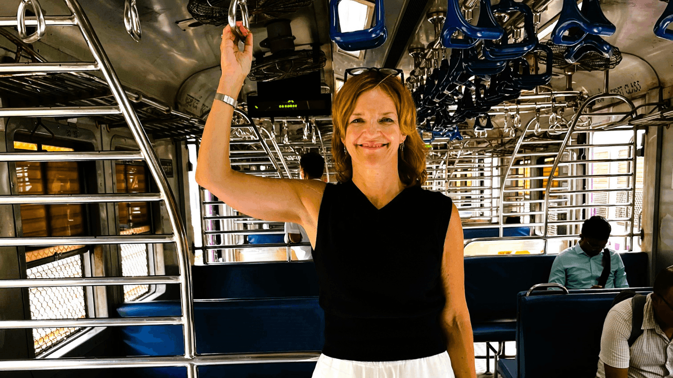 Woman smiling while standing inside a train carriage holding an overhead handle