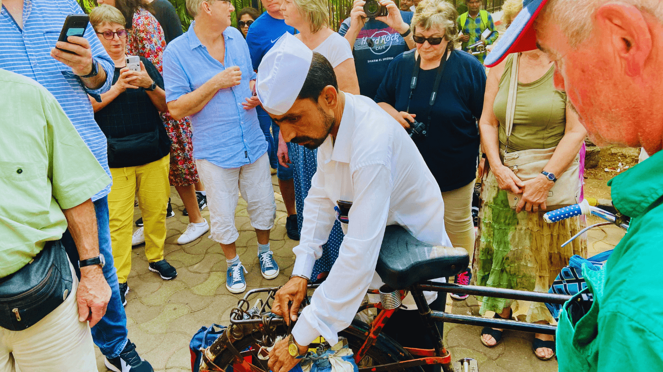 Mumbai dabbawala demonstrating lunchbox delivery system to tourists during a guided city tour